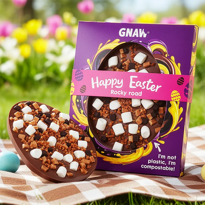 Chocolate Rocky road with marshmallows and a purple 'Happy Easter' GNAW packaging on a checkered blanket with flowers background.