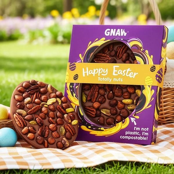 Chocolate Easter egg with nuts and packaging labeled GNAW 'Happy Easter Totally Nuts' on a picnic setting.